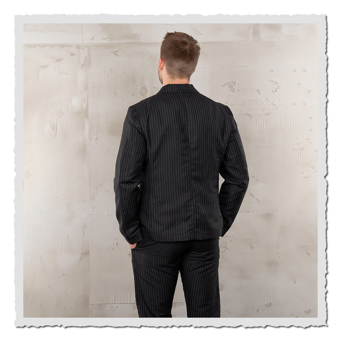 Rückansicht eines Models im schwarzen Nadelstreifen-Sakko, Studioaufnahme vor hellem Hintergrund.